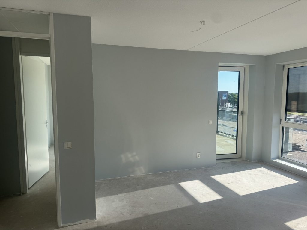 Lege kamer in een nieuw appartement met lichtgrijze wanden en een balkondeur