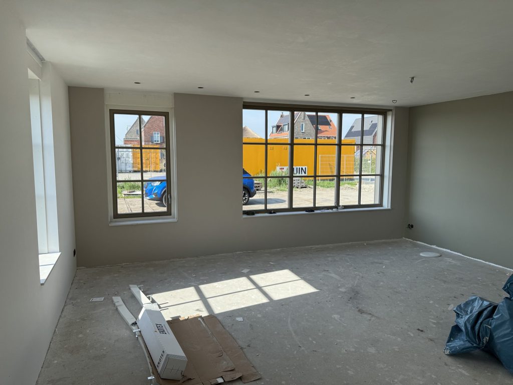 Woonkamer in een nieuwe woning met wanden in een warme grijstint en grote ramen