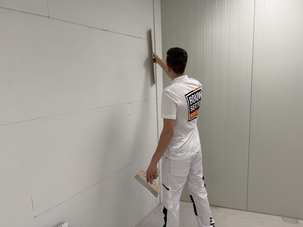 Vakman van Bouwsector Nederland maakt een muur vlak met een spaan voordat er behang op gaat